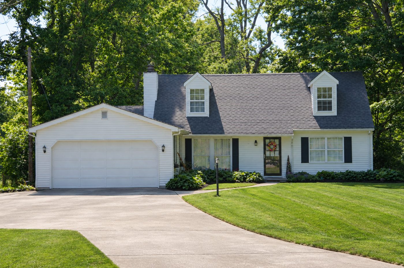 White cape-style home with a neatly mowed lawn and curved driveway