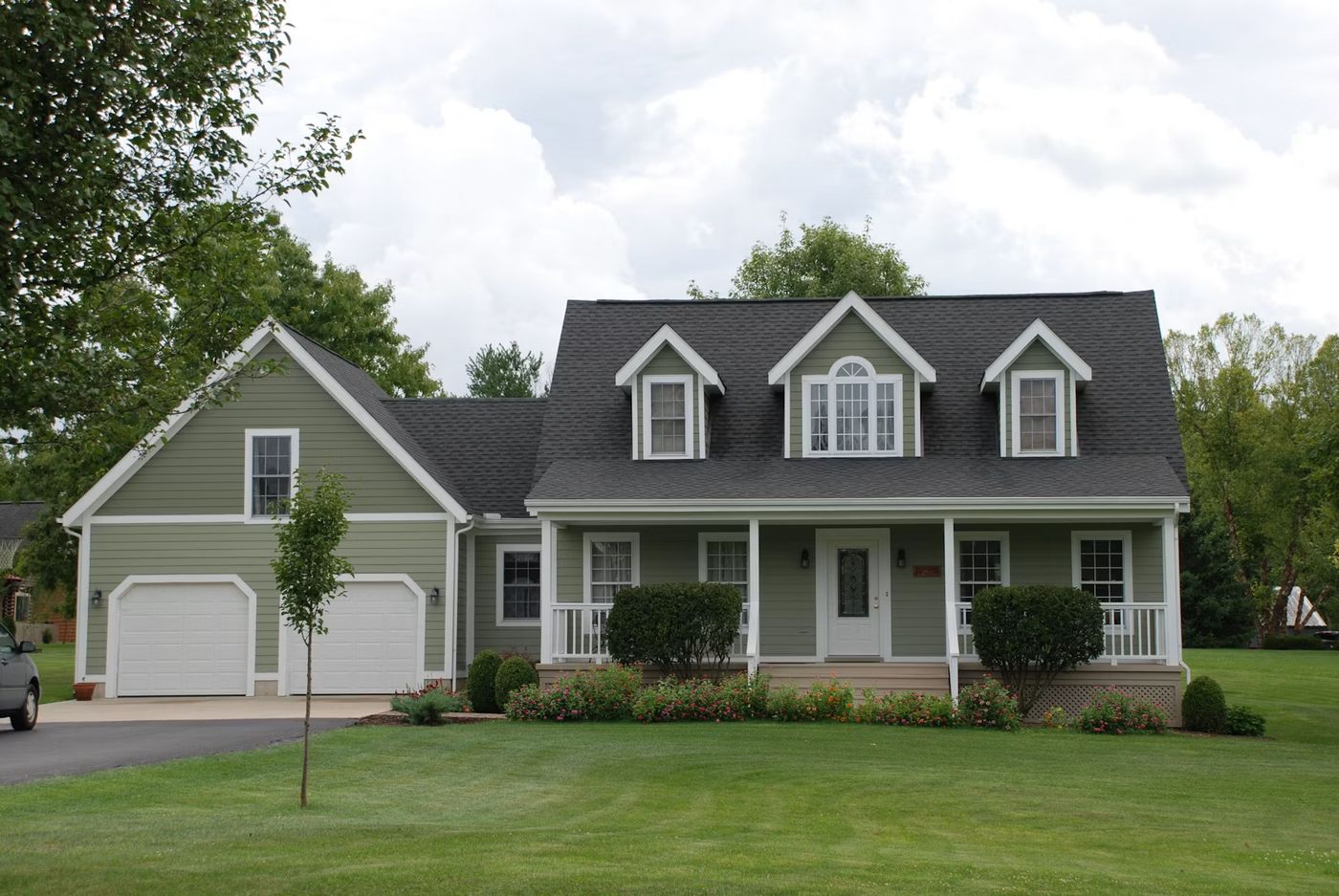 Green cape-style home with a front porch and manicured lawn
